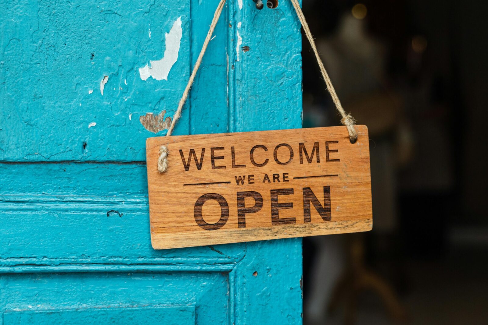 A rustic wooden 'Welcome We Are Open' sign hanging on a vibrant blue door.